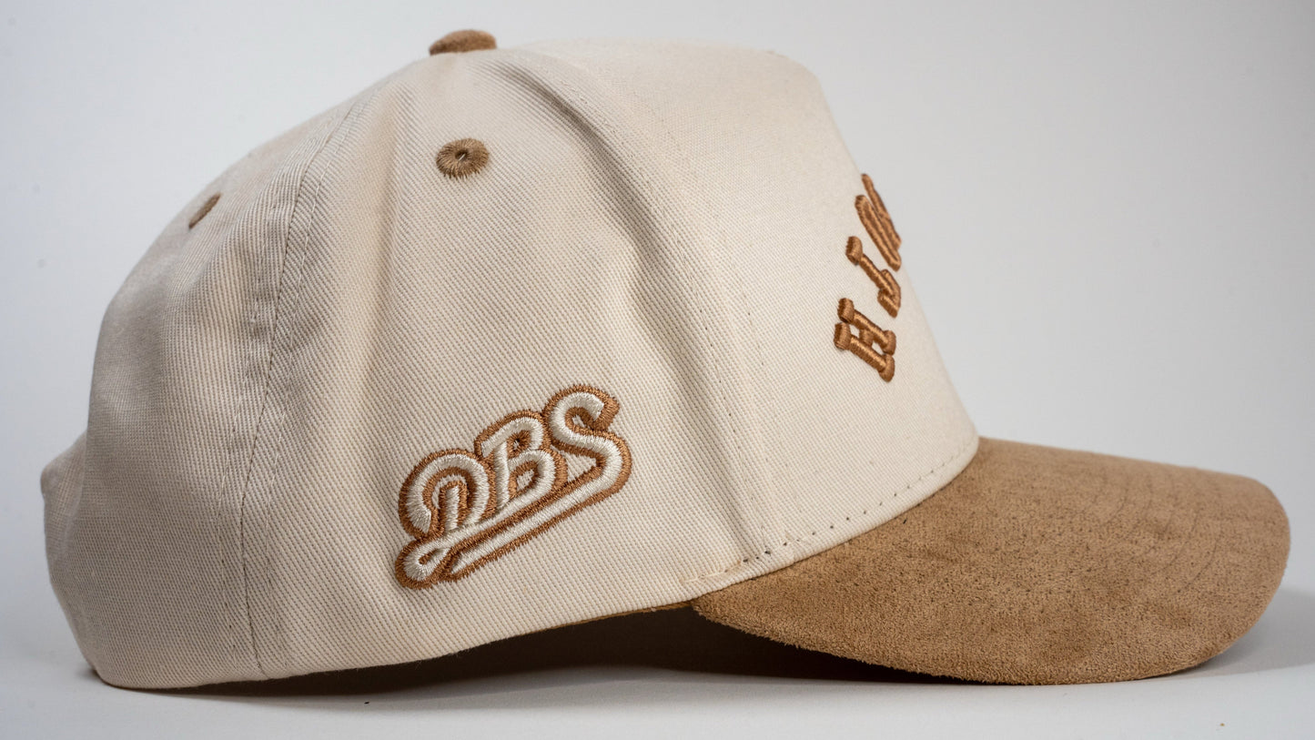 A cream baseball cap with beige brim displays mirrored letters 'REHOBOTH' and a beige embroidered logo on the side.
