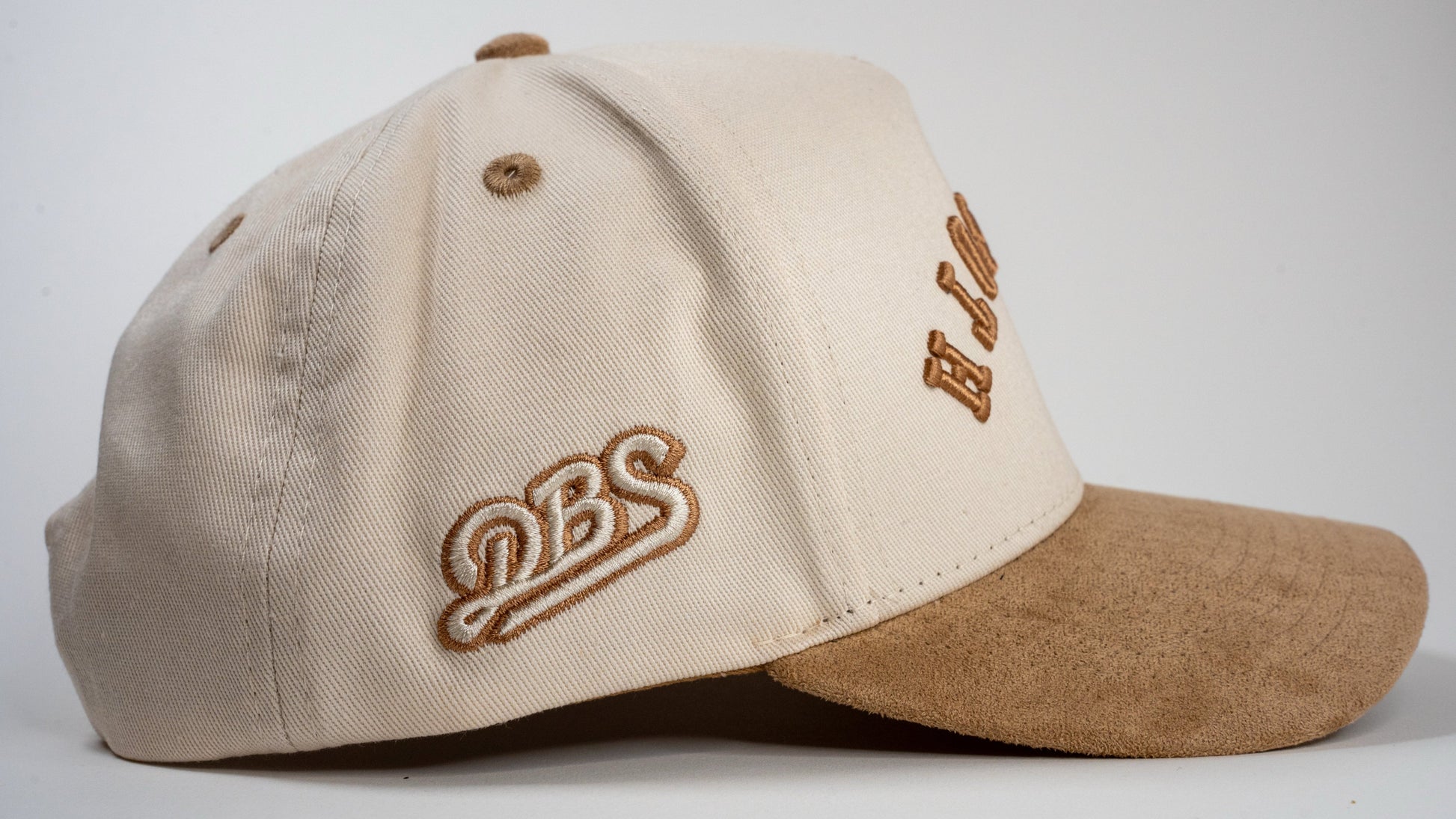 A cream baseball cap with beige brim displays mirrored letters 'REHOBOTH' and a beige embroidered logo on the side.