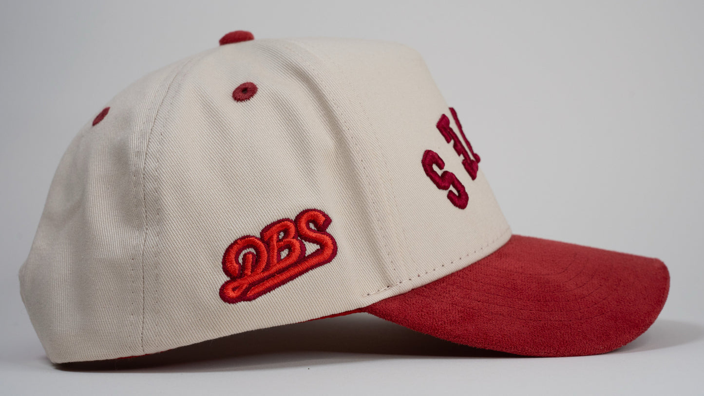 A cream baseball cap with red brim displays mirrored letters 'LEWES' and a red embroidered logo on the side.