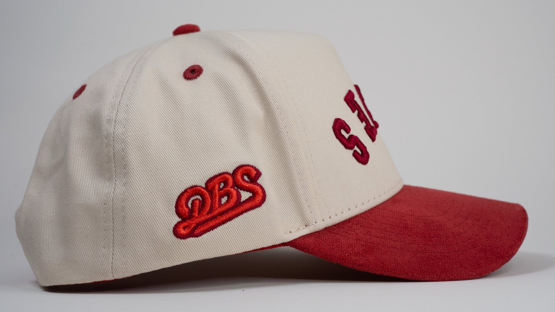 A cream baseball cap with red brim displays mirrored letters 'LEWES' and a red embroidered logo on the side.