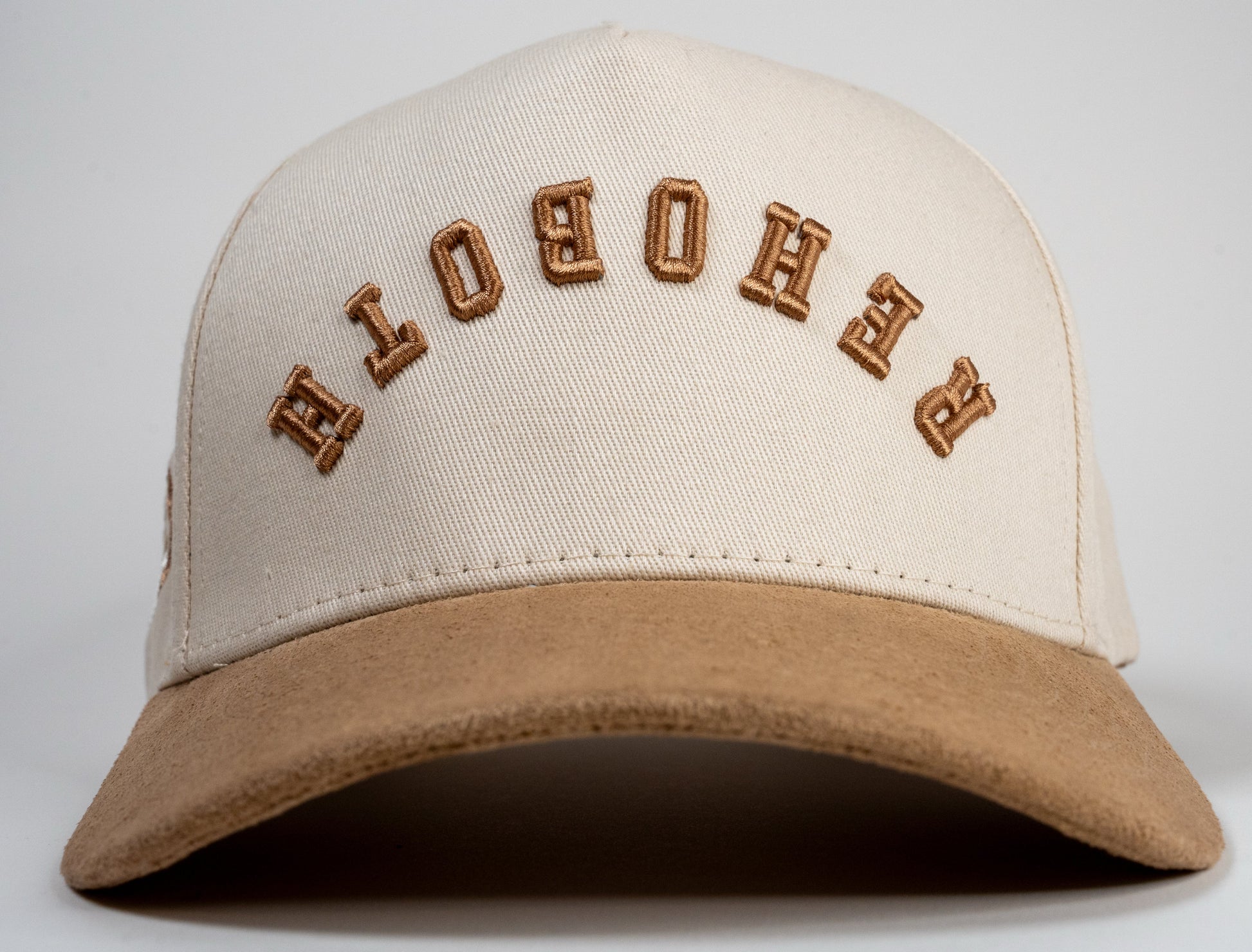 A cream baseball cap with beige brim displays mirrored letters 'REHOBOTH' and a beige embroidered logo on the side.