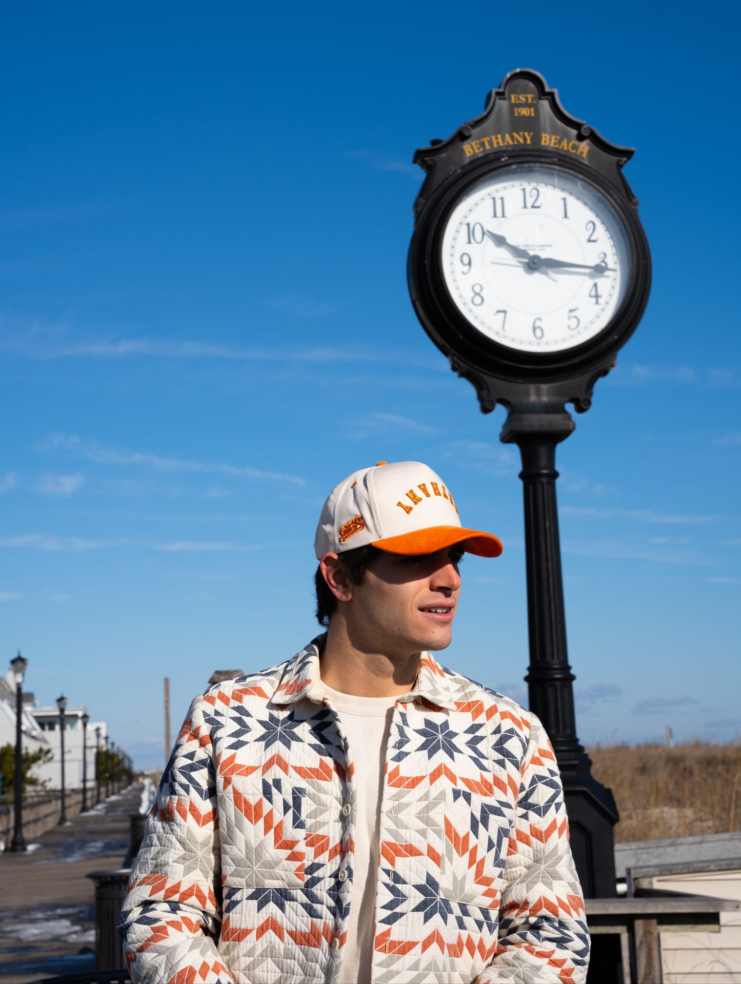 A cream baseball cap with an orange brim displays mirrored letters 'BETHANY' and an orange embroidered logo on the side.